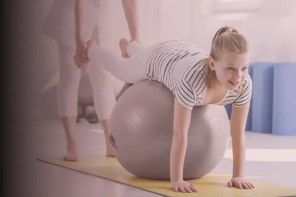 Kind übt mit einer Therapeutin auf dem Gymnastikball